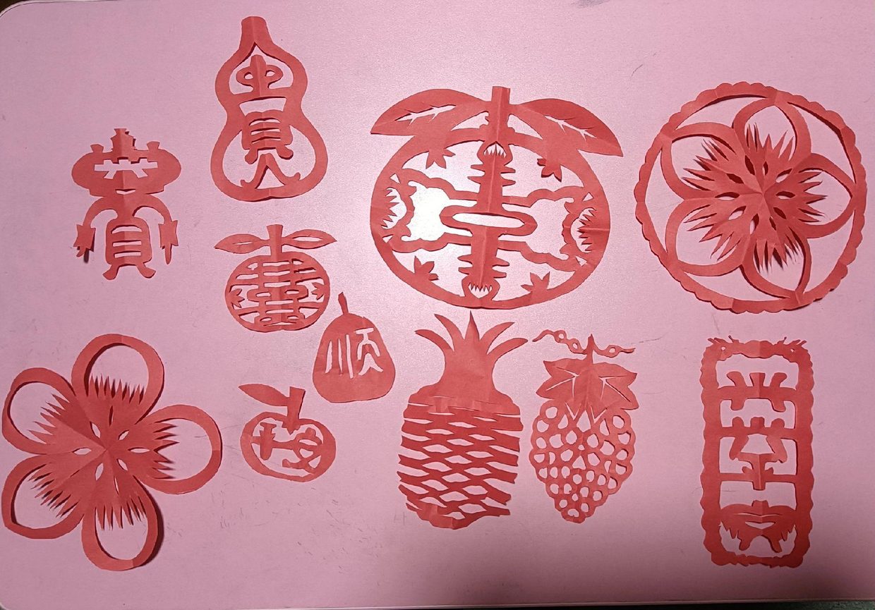 一组红纸剪纸：葫芦、桃、菠萝、葡萄与「平安」字样，平铺成一版。图源：抖音 @潮州剪纸黄朝阳（跃然斋文化传播），2023 年 9 月 29 日。